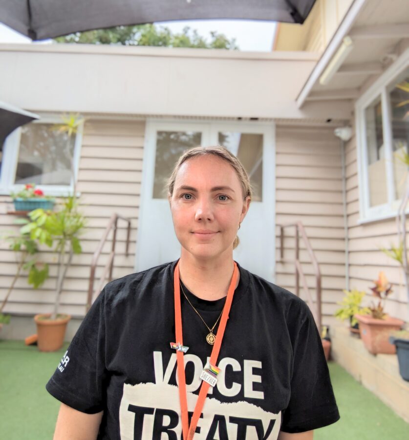 A woman with blond hair tied back, she is wearing a black shirt and an orange lanyard.