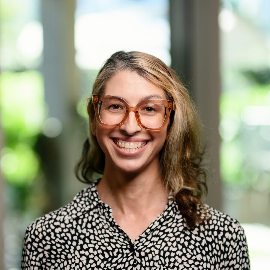 A woman with long, light hair and large rim glasses smiling at the camera.