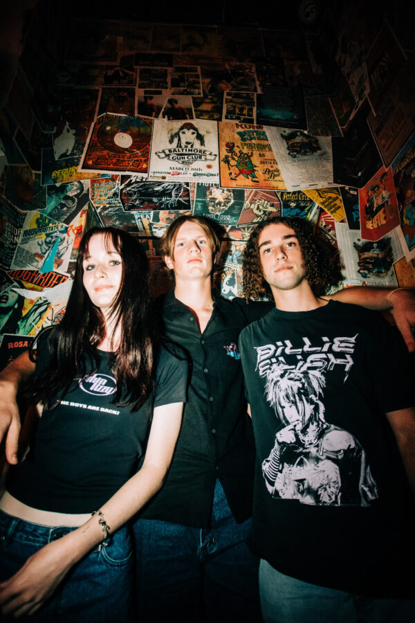 3 people standing in front of a wall filled with band posters